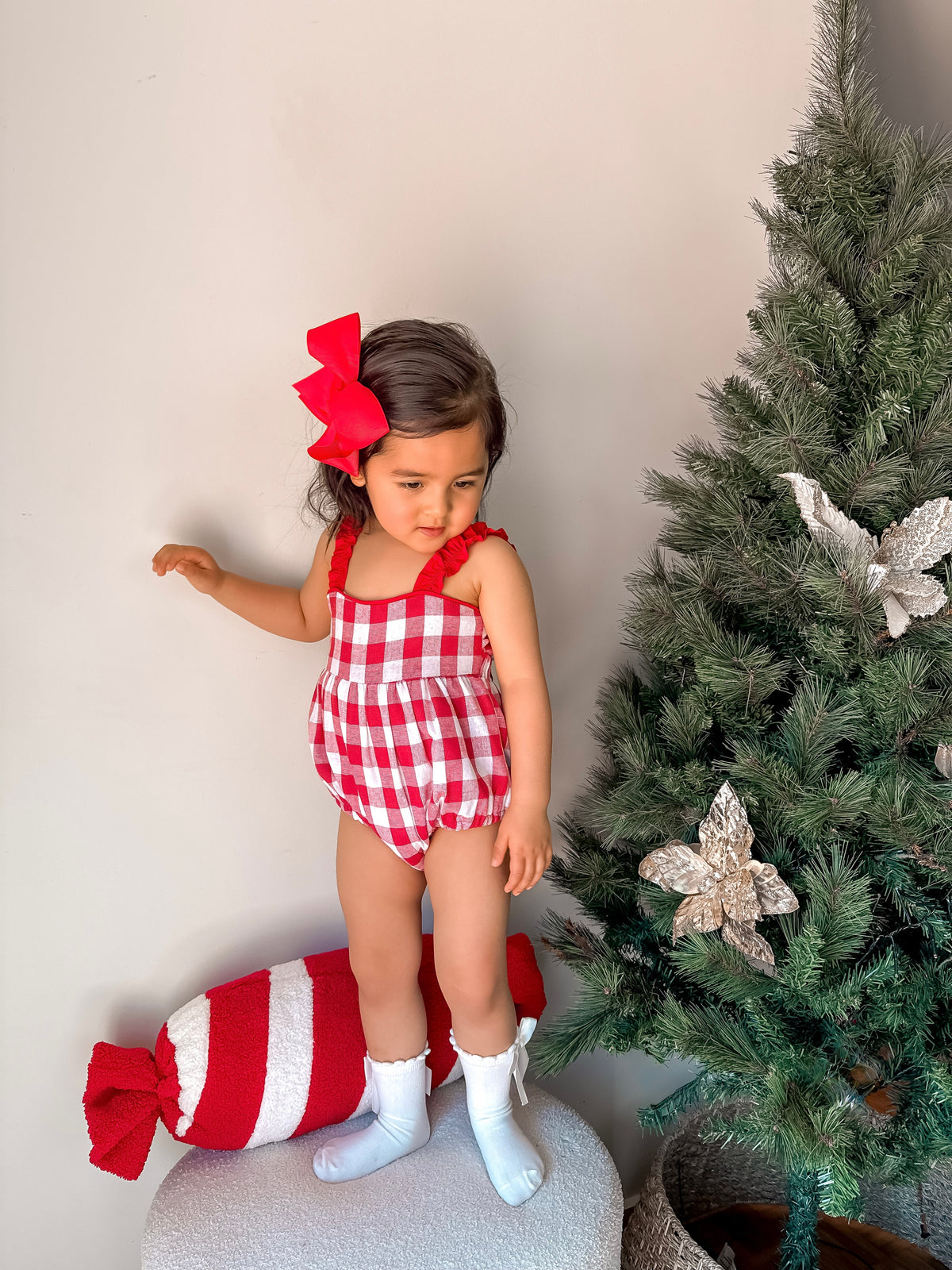 Child in red checkered outfit with a large candy and Christmas tree in the background