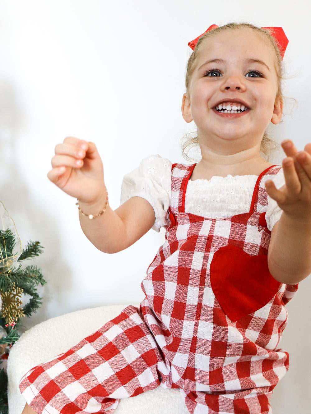 Child wearing a red and white checkered outfit with a heart design, sitting on a white surface.