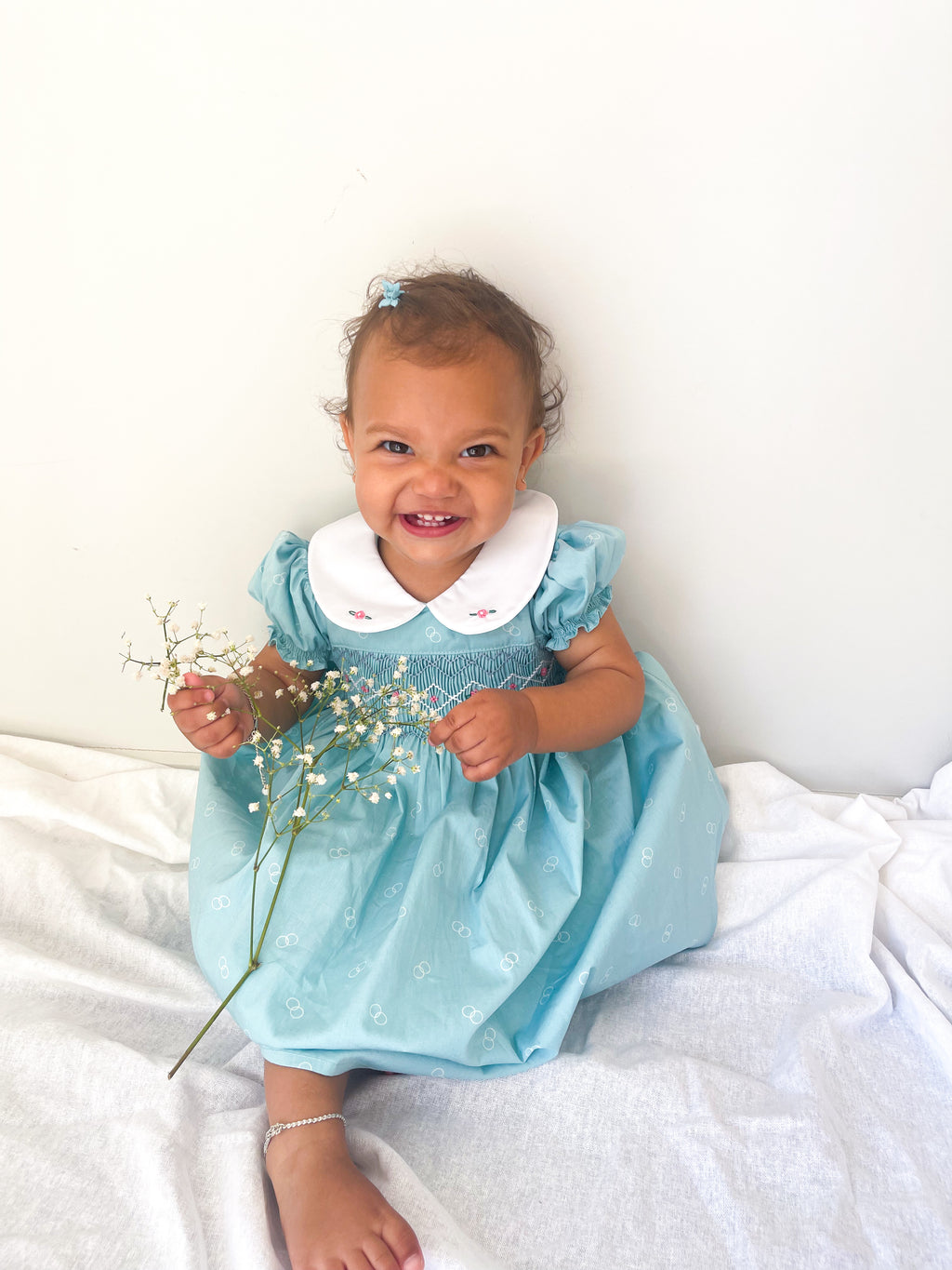 Baby wearing the Hand-smocked buebell Dress . Its a light blue dress with blue and white hand smocking with rose bud embroidery