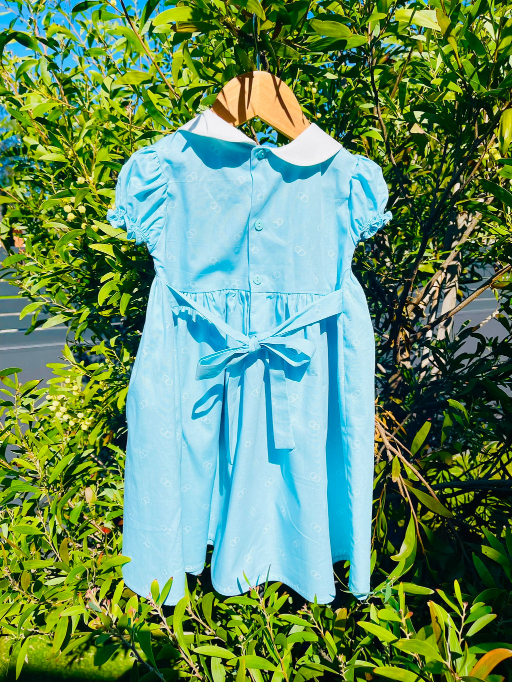 Back of the hand-smocked bluebell dress, it has buttons on blue at the back with a blue bow stash