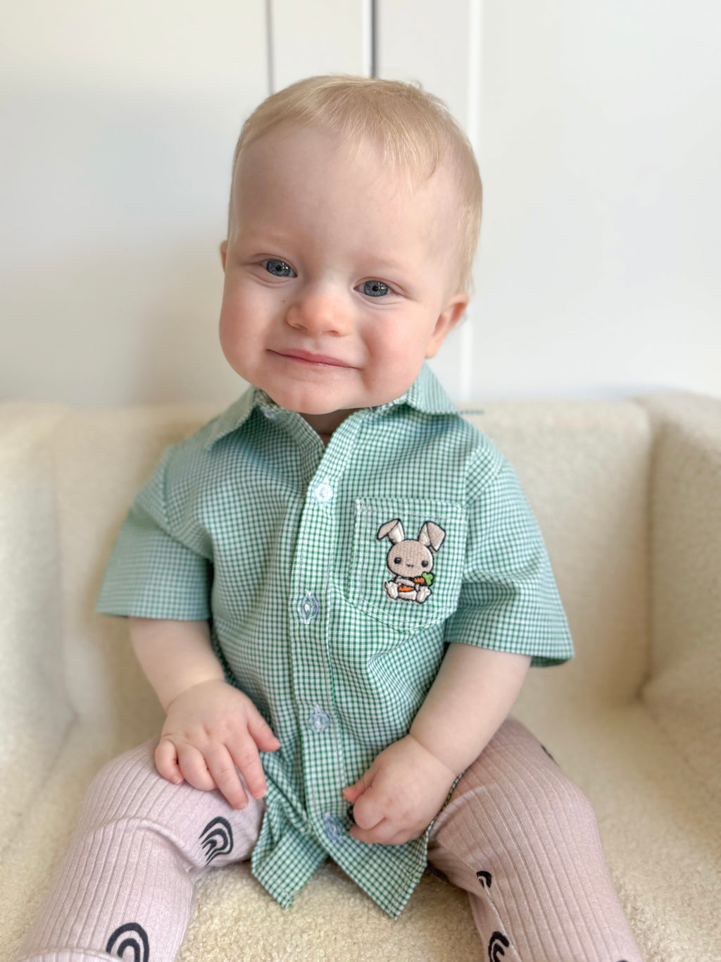 Baby wearing a green checkered shirt with a bunny design on a white couch.