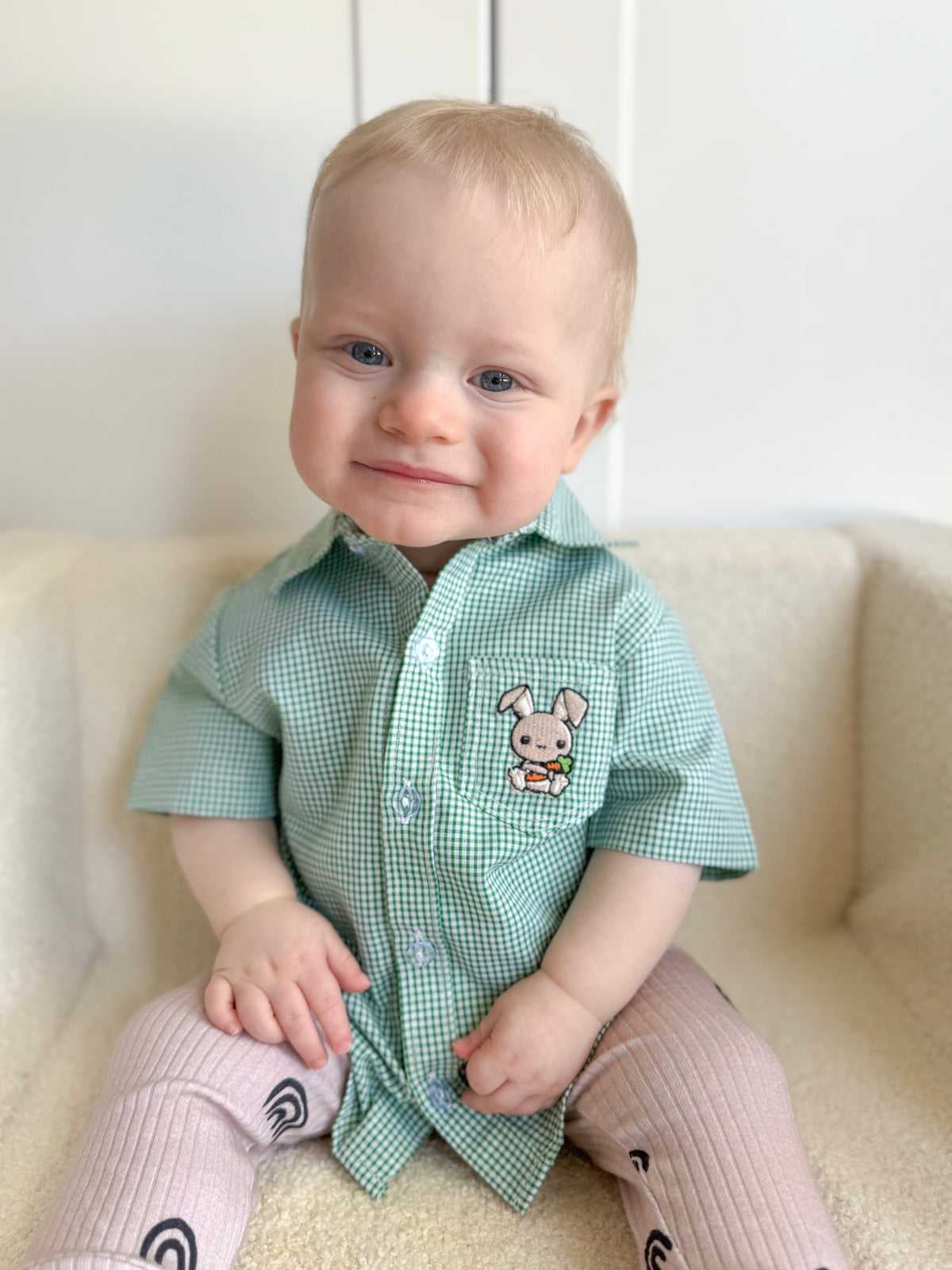 Baby wearing a green checkered shirt with a bunny design on a white couch.