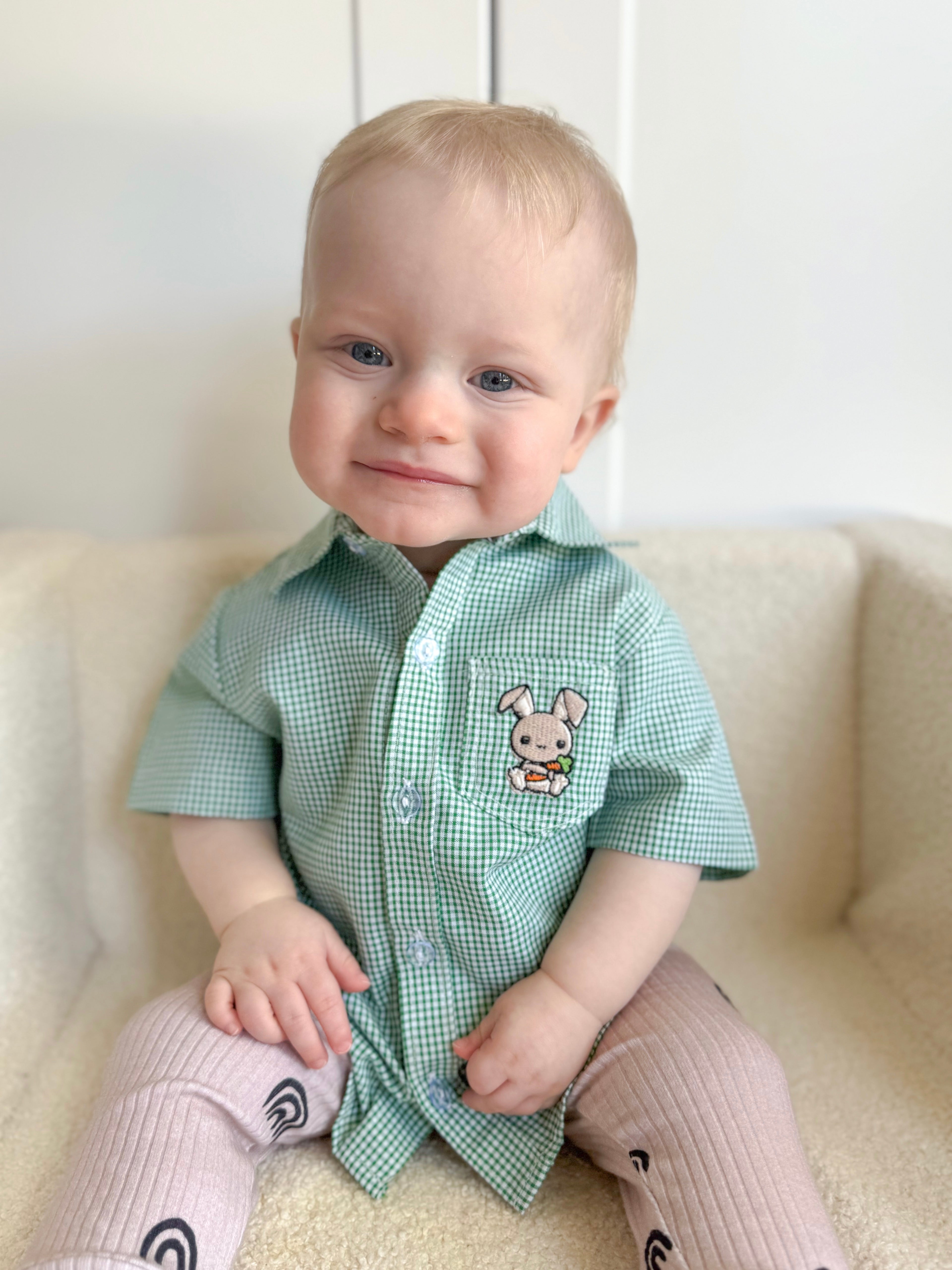 Baby wearing a green checkered shirt with a bunny design on a white couch.