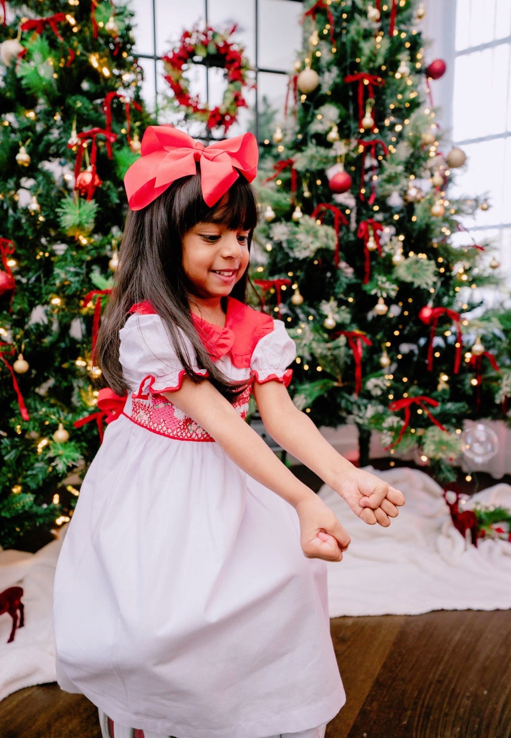 Young girl in a festive dress standing in front of decorated Christmas trees.