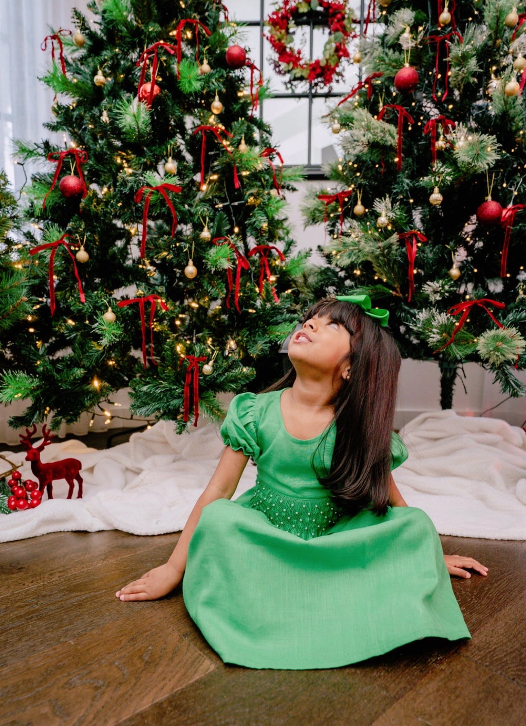 Girl sitting in front of Christmas trees wearing a green hand smocked dress
