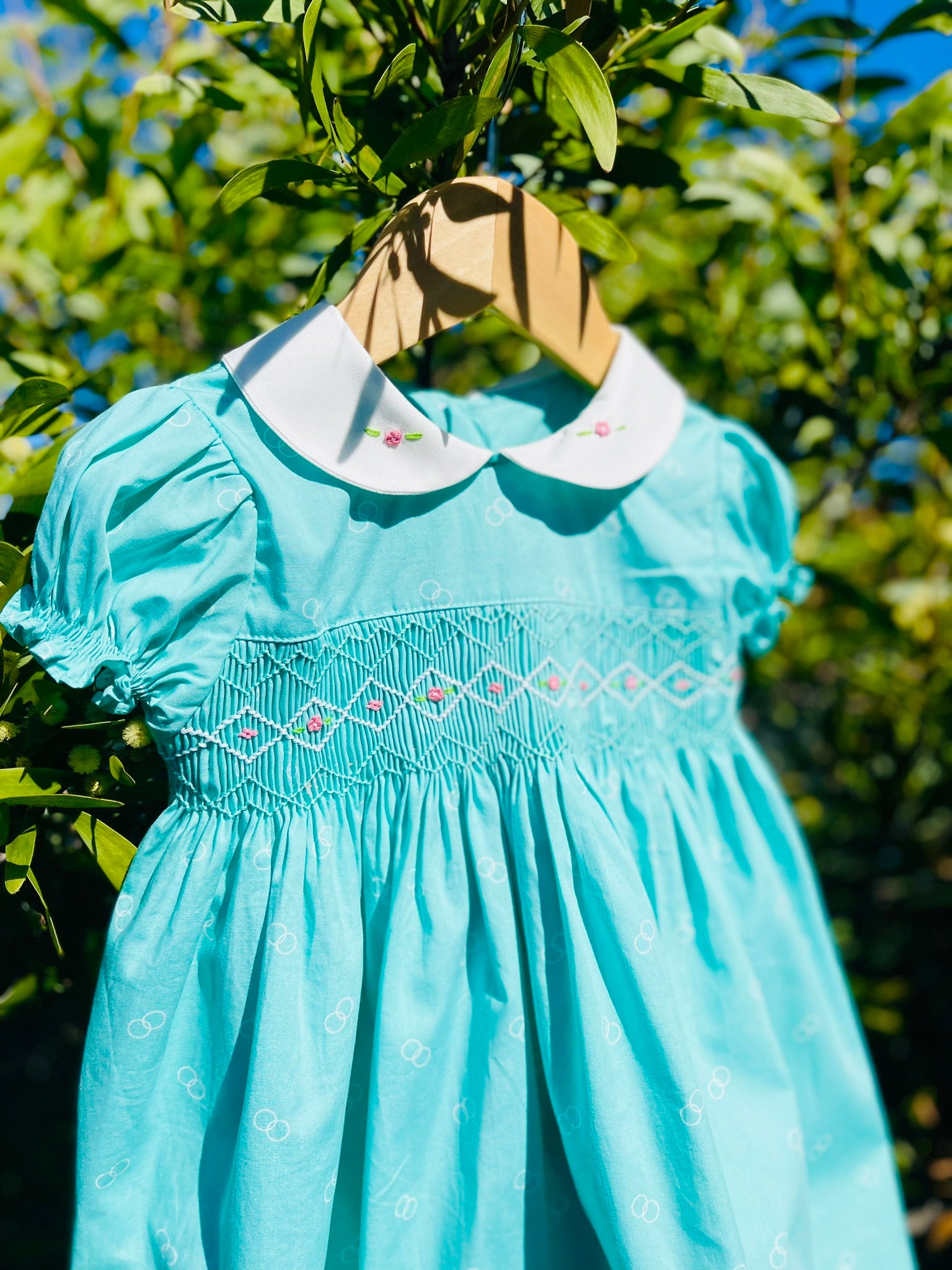 Side and close up photo of the Hand-smocked Emerald Rose Dress. Emerald green and white handsmocking with pink rose bud embrodiery. White collar with one pink rose bud embrodiery on each collar.Dress is a green colour.