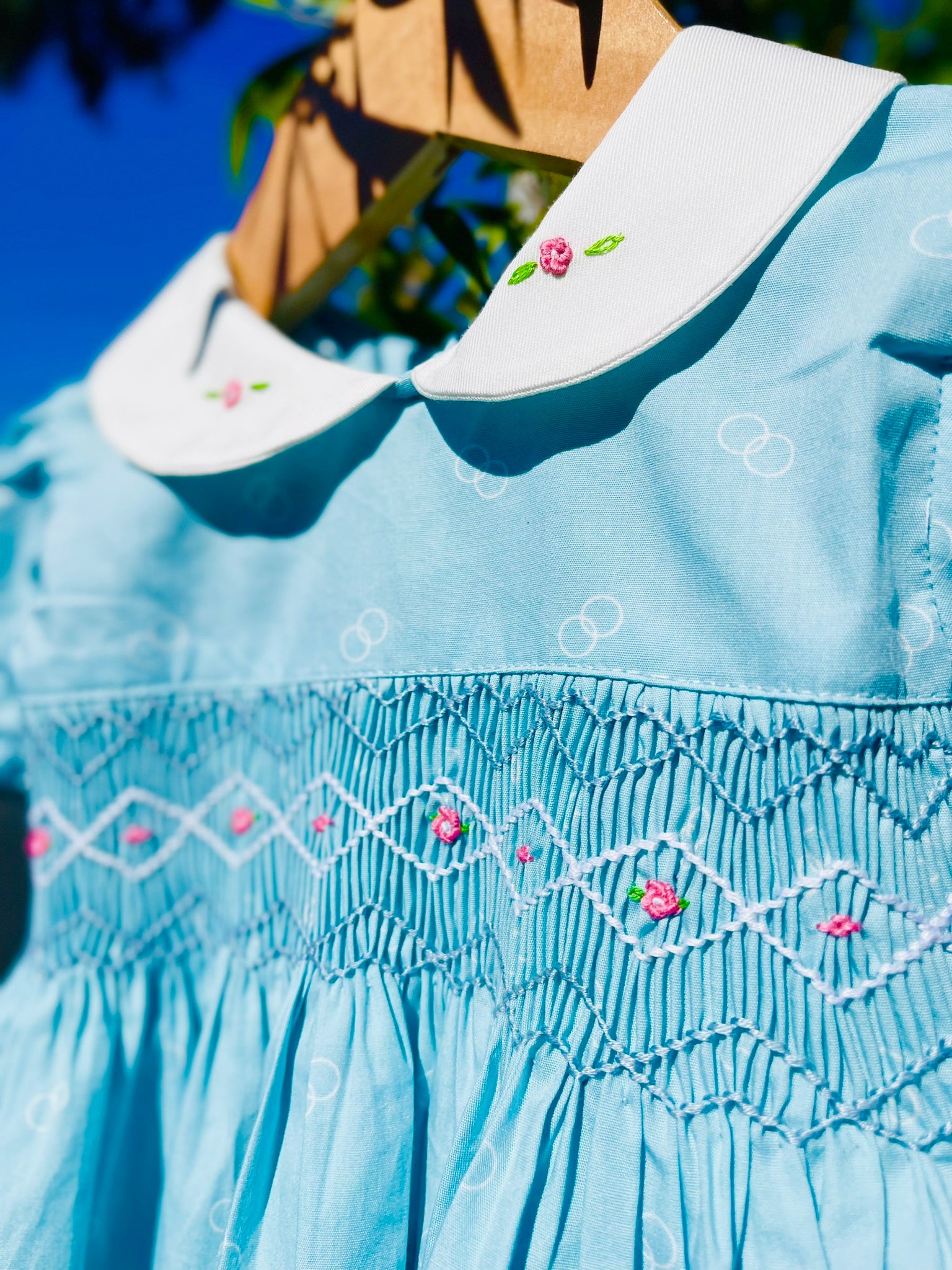 Close up of the handsmocking in the bluebell dress. Pink rose bud embroidery on blue and white handsmocking. White colour with two small rose bud embroidery
