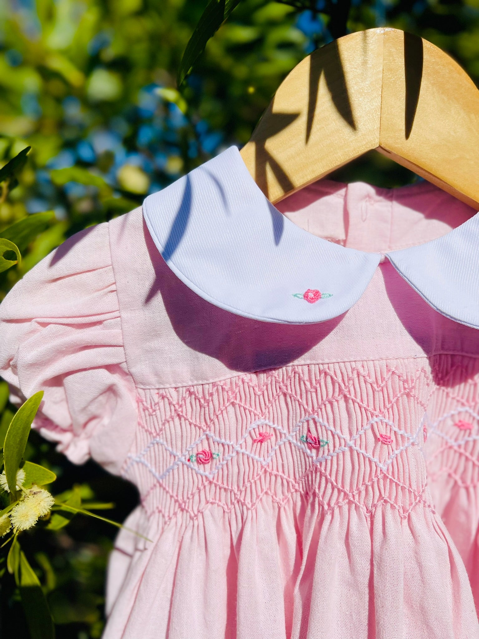 Close up photo of the top part and side of the hand-smocked pink sakura dress. Light Pink Dress that has Pink and white handsmocking with dark pink rose bud embroidery. White collar with one pink rose bud embroidery on each collar. Dress is a light pink colour.