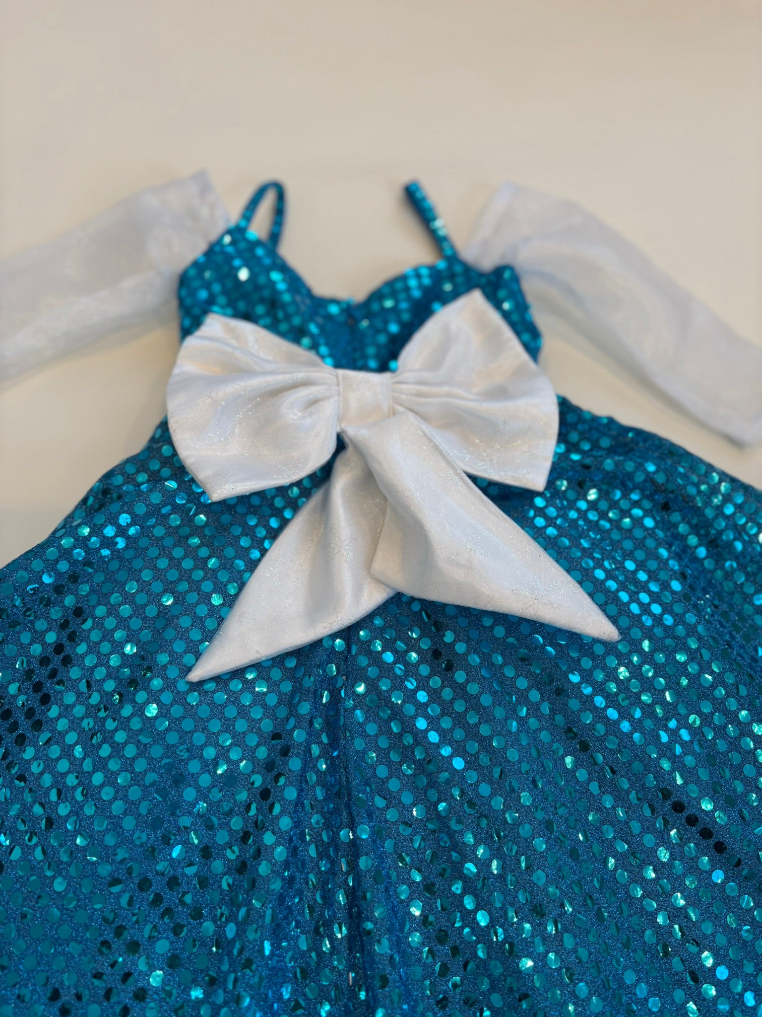 Blue sequin dress with a large white bow on a beige background