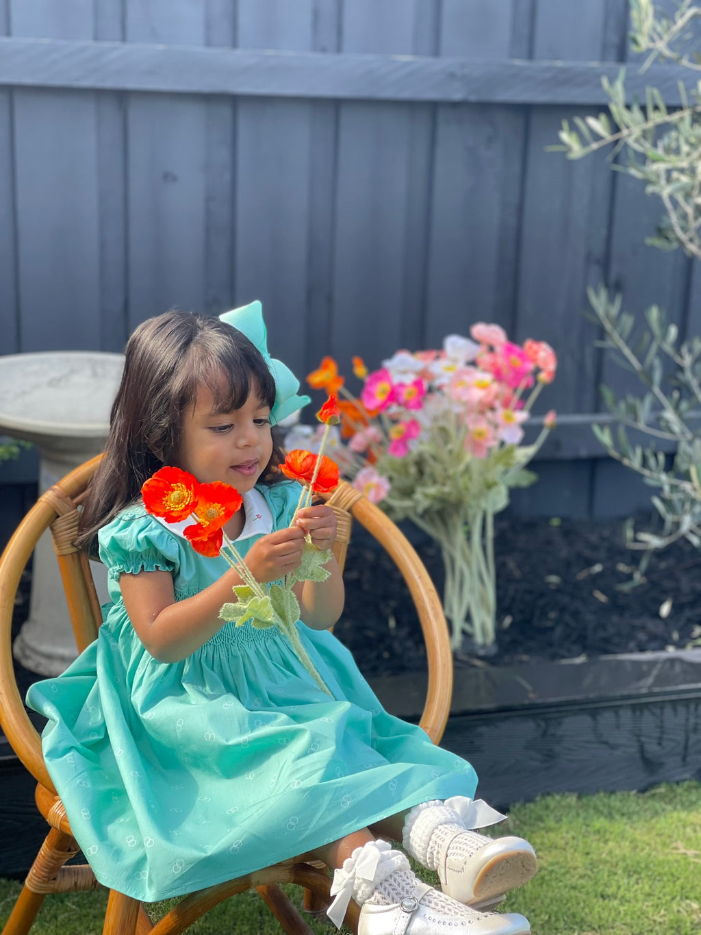 Girl Toddler wearing the Hand-smocked Emerald Rose Dress. Emerald green and white hand-smocking with pink rose bud embroidery. White collar with one pink rose bud embroidery on each collar. Dress is a green colour.