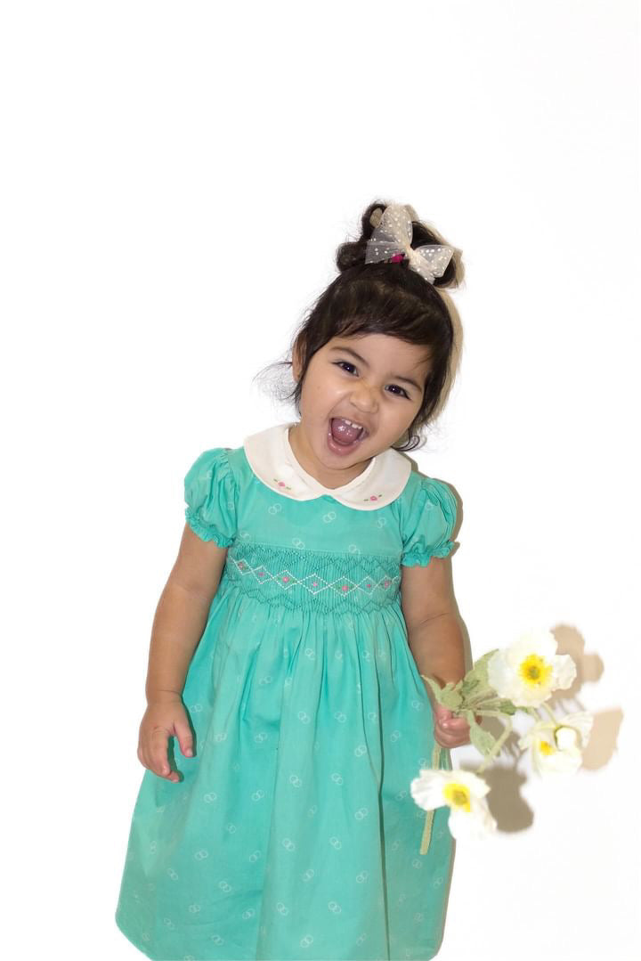 Girl Toddler wearing the Hand-smocked Emerald Rose Dress. Emerald green and white handsmocking with pink rose bud embrodiery. White collar with one pink rose bud embrodiery on each collar.Dress is a green colour.