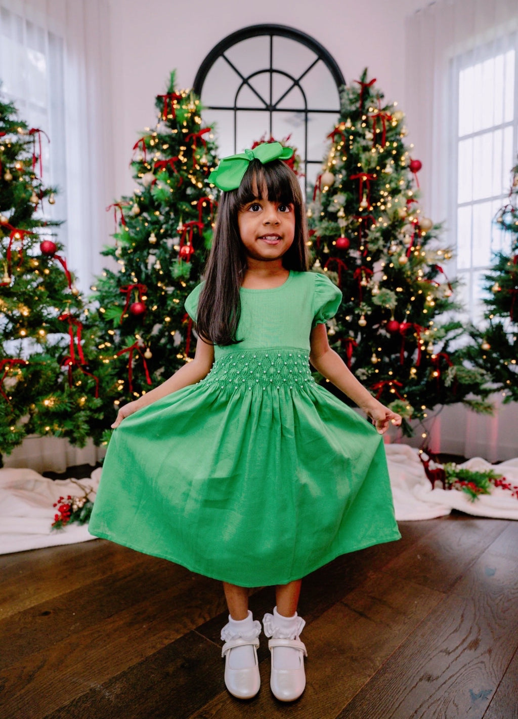 Young girl in a green dress standing in front of Christmas trees.