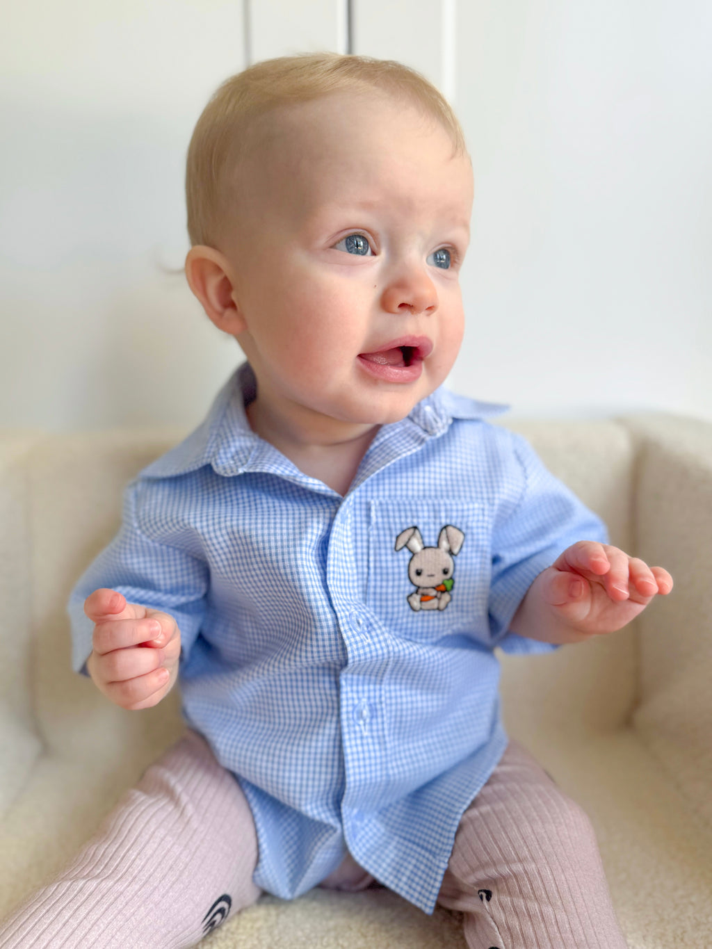 Baby wearing a light blue checkered shirt with a bunny design on a white couch.