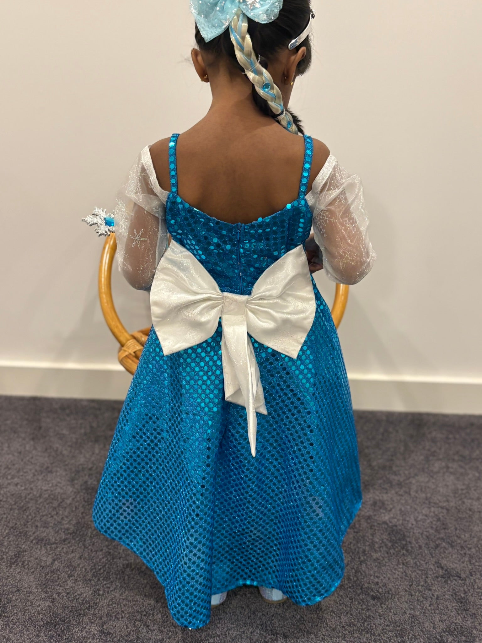 Child wearing a blue dress with a white bow, standing against a plain background