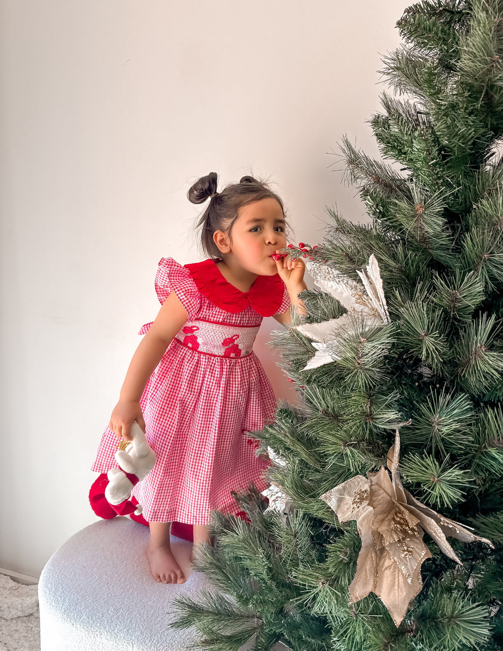 Young girl in a red dress standing next to a decorated Christmas tree.