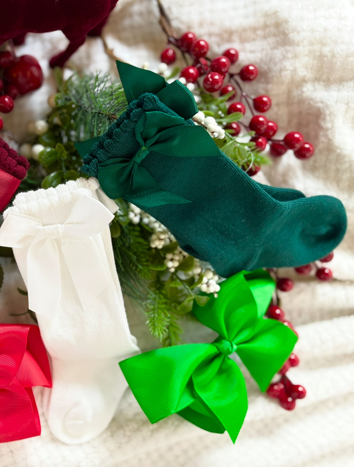 Green socks with green bows on a textured surface with red berries and green leaves.