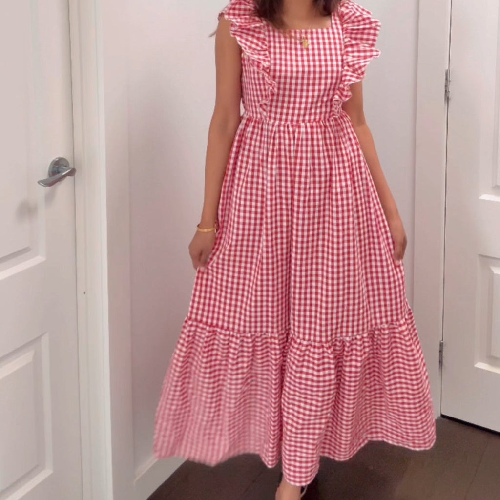 Woman wearing a red and white checkered dress in a room with white walls and a door.