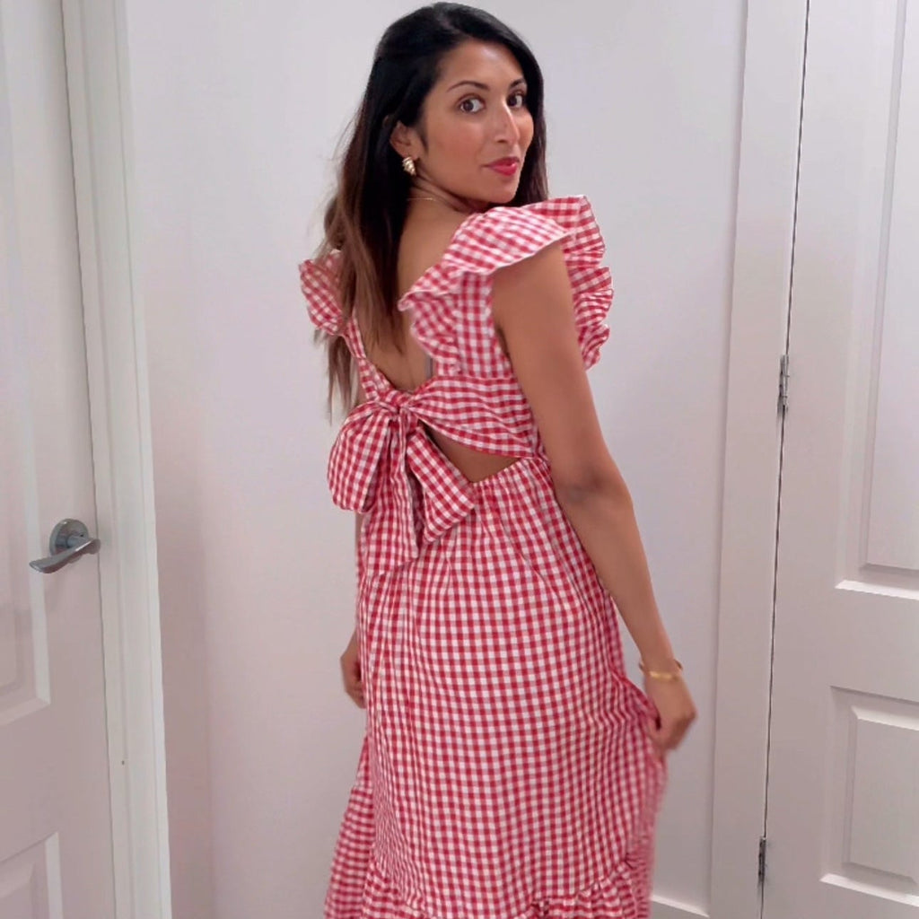 Woman wearing a red and white checkered dress with a back bow, standing in a room with white doors.