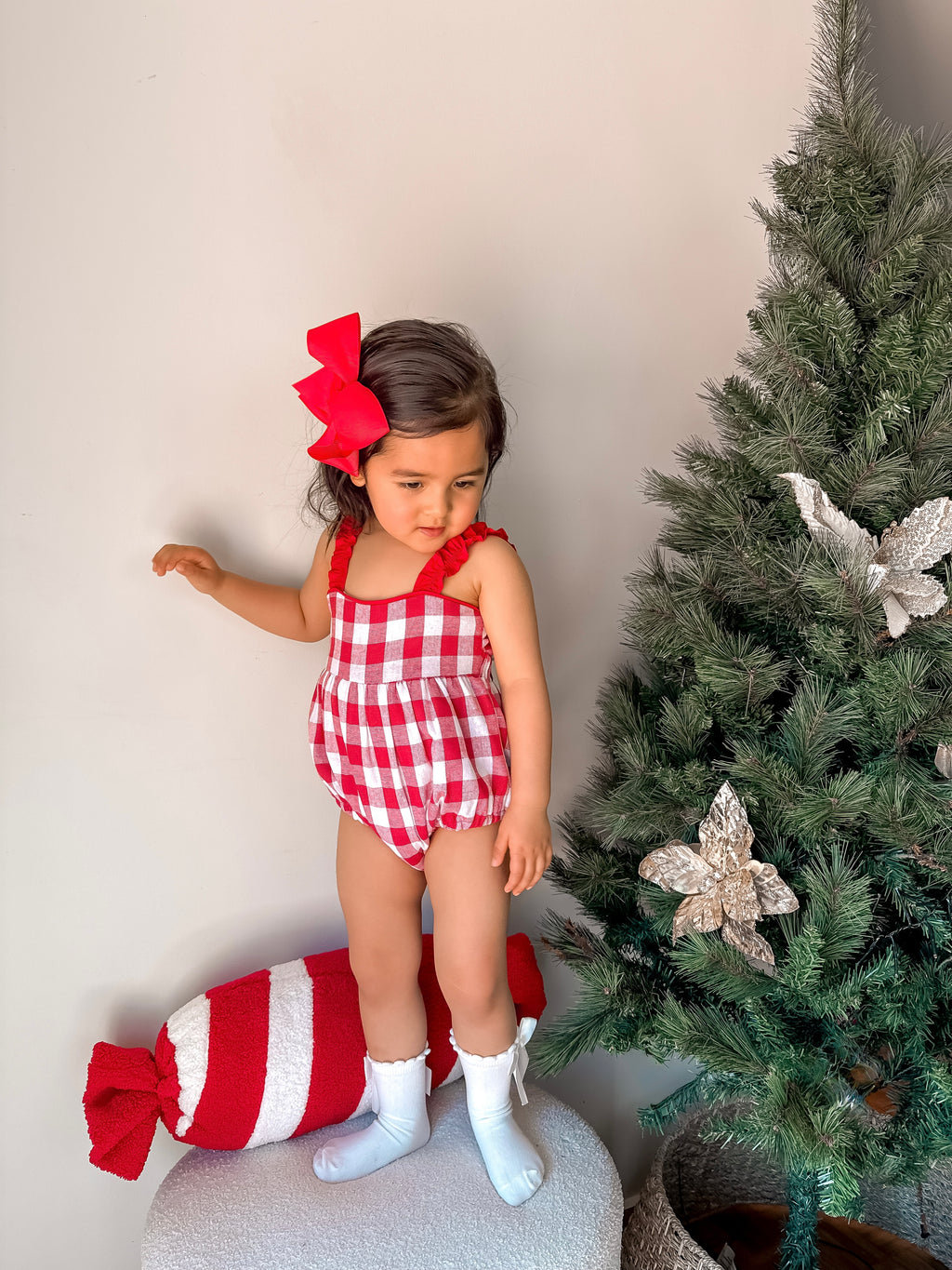 Child in red checkered outfit with a large candy and Christmas tree in the background