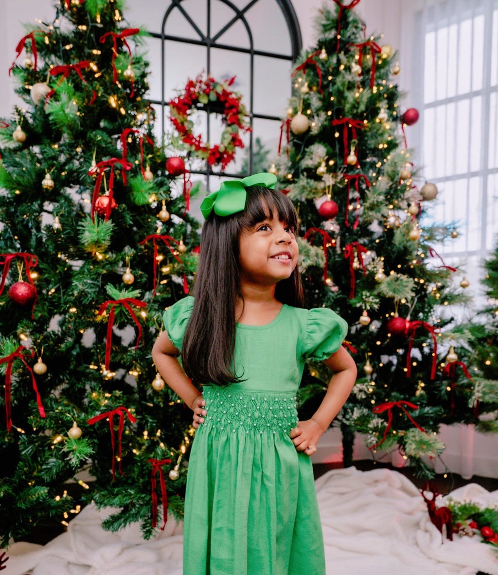 Young girl in a green dress standing in front of Christmas trees with decorations.