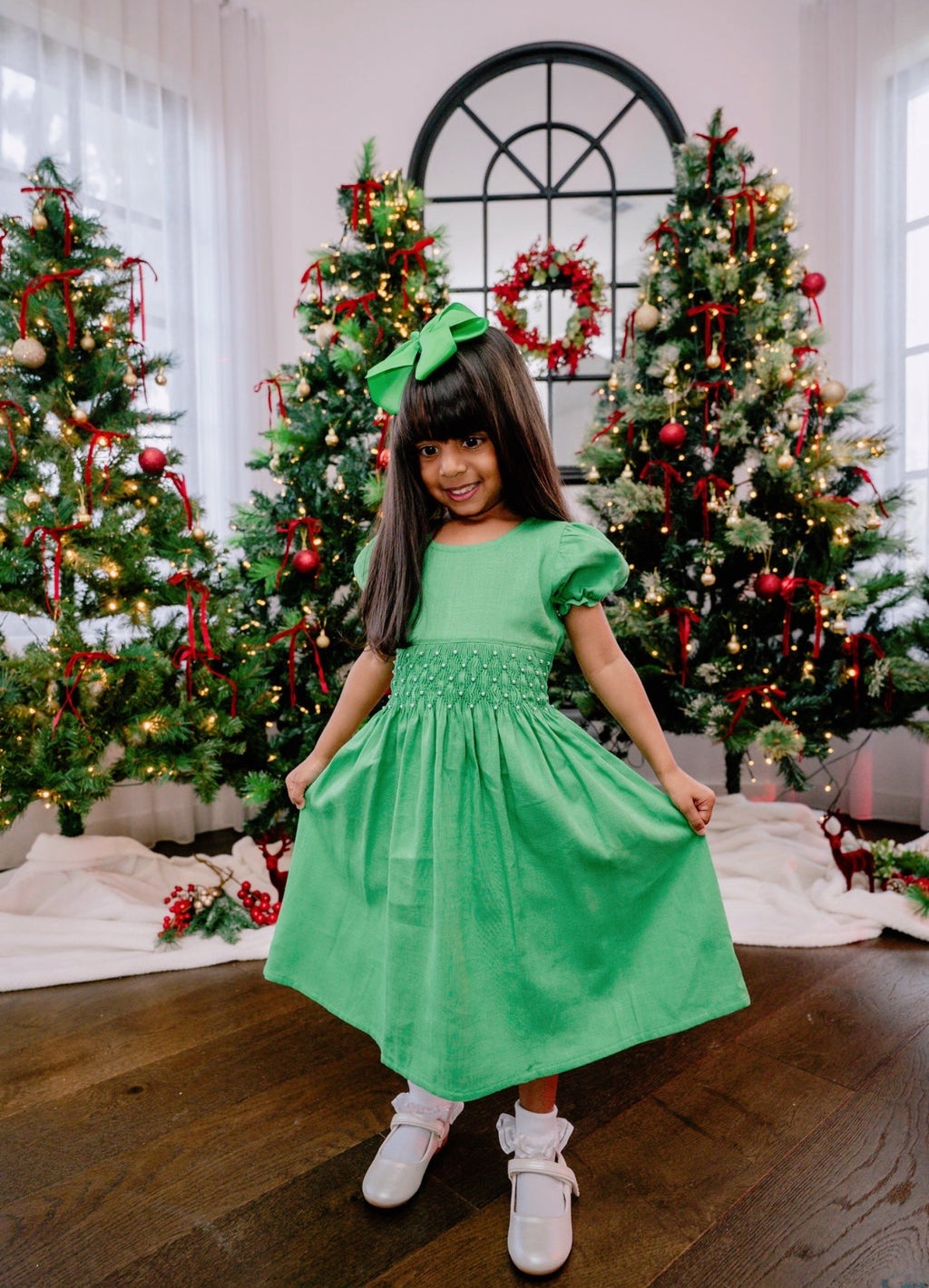 Girl standing in front of Christmas trees wearing a green hand smocked dress