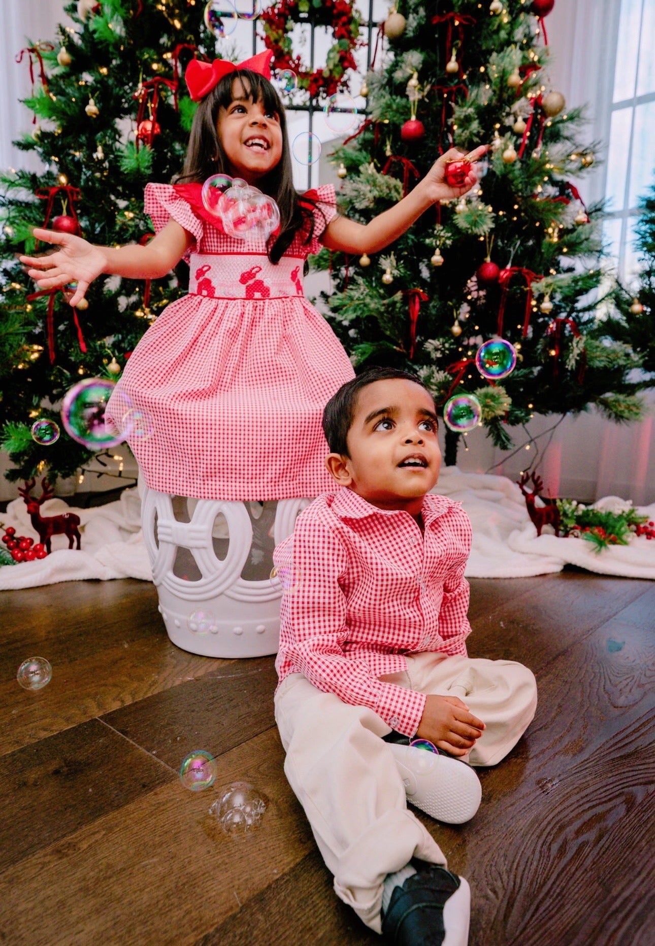 Two children in matching red and white outfits in front of a decorated Christmas tree.