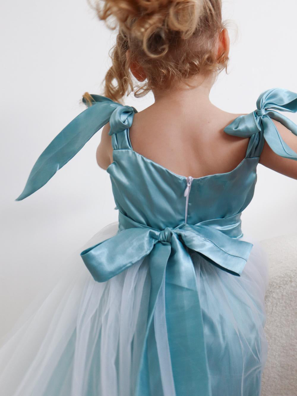 Child wearing a light blue dress with large bows on a plain background