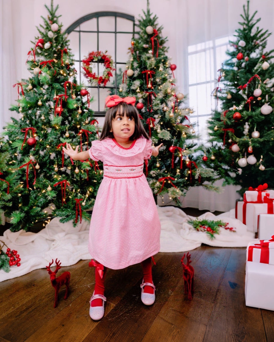 Young girl in a pink dress standing in front of Christmas trees and presents.