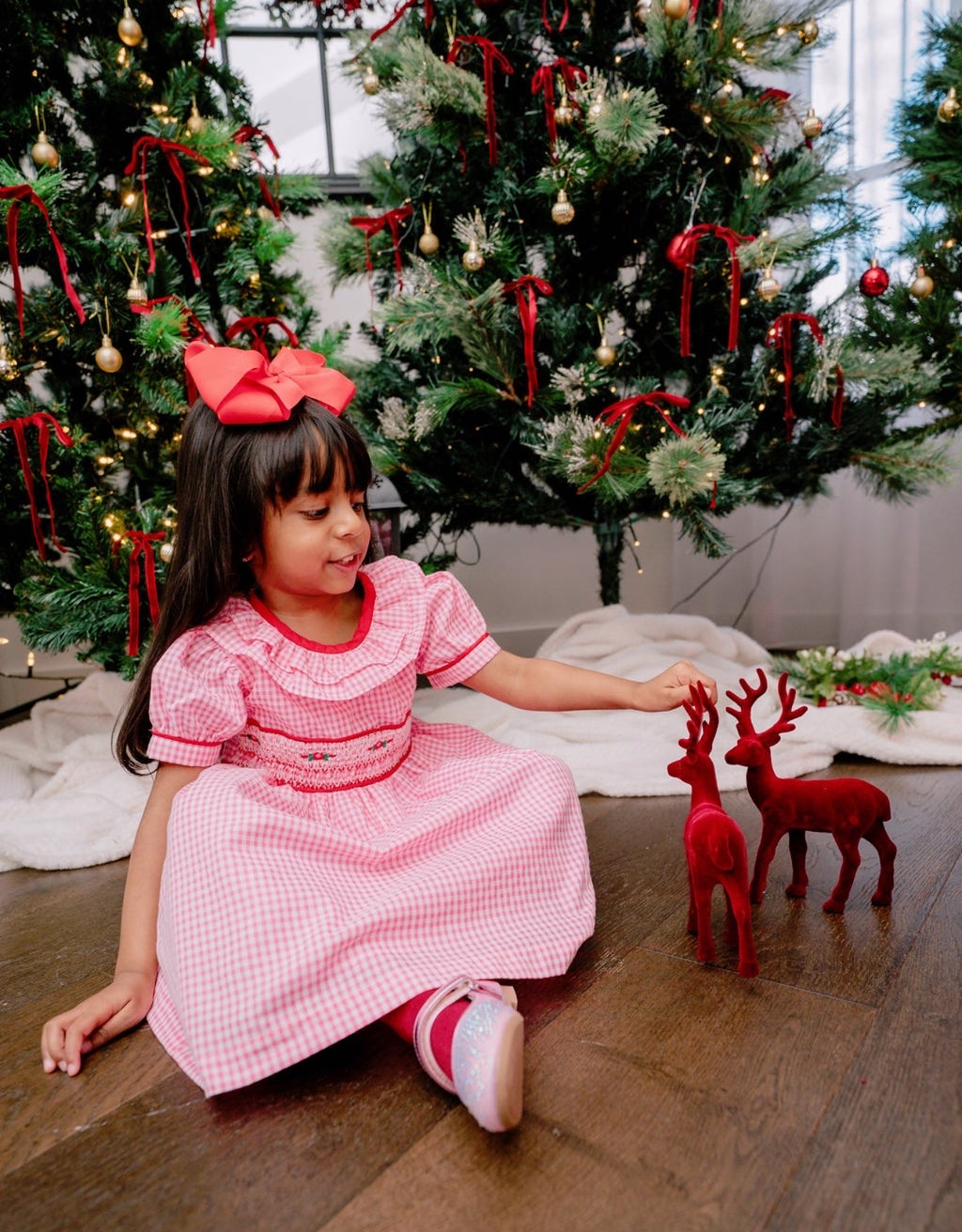 Young girl in a pink dress sitting on the floor with Christmas trees in the background