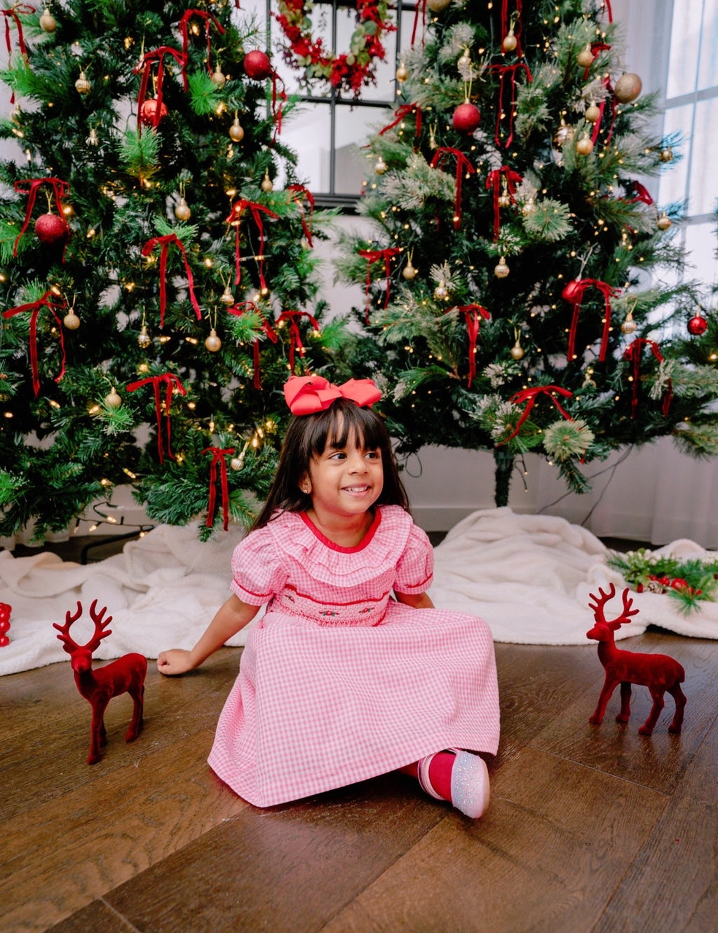 Young girl in a pink dress sitting in front of a decorated Christmas tree with ornaments and lights.