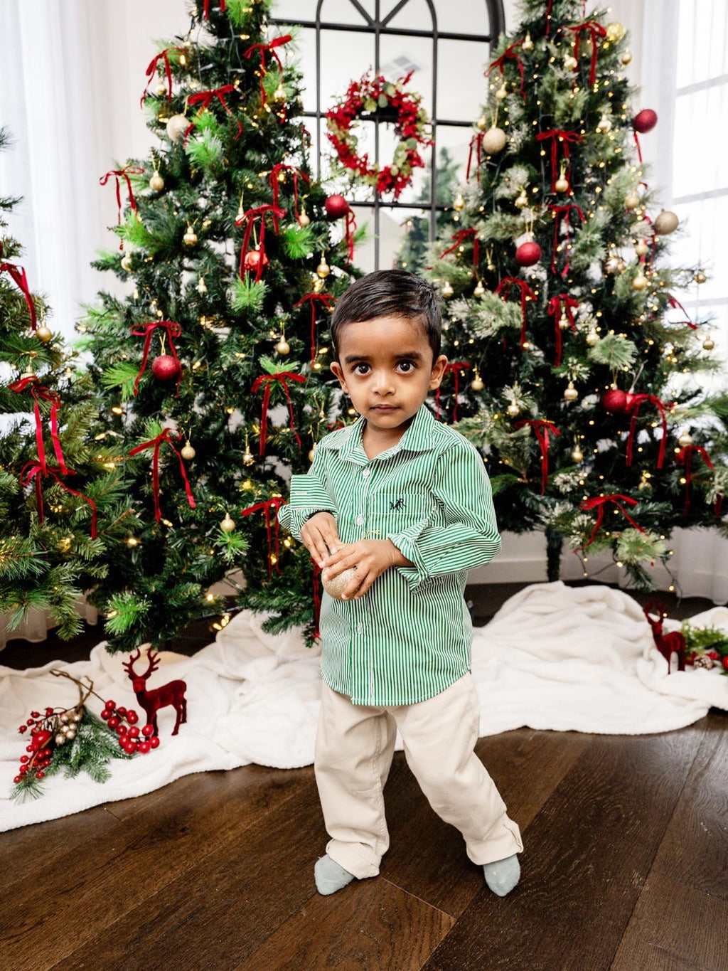 Child standing in front of a decorated Christmas tree with red ribbons and lights.