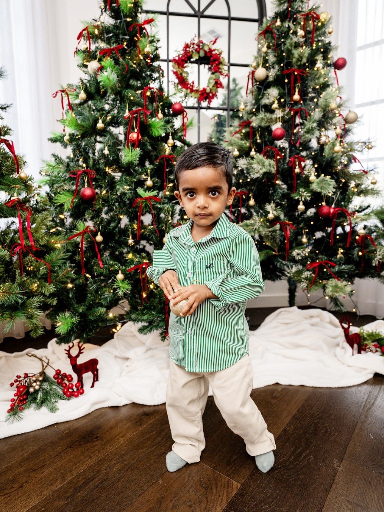 Child standing in front of a decorated Christmas tree with red ribbons and lights.