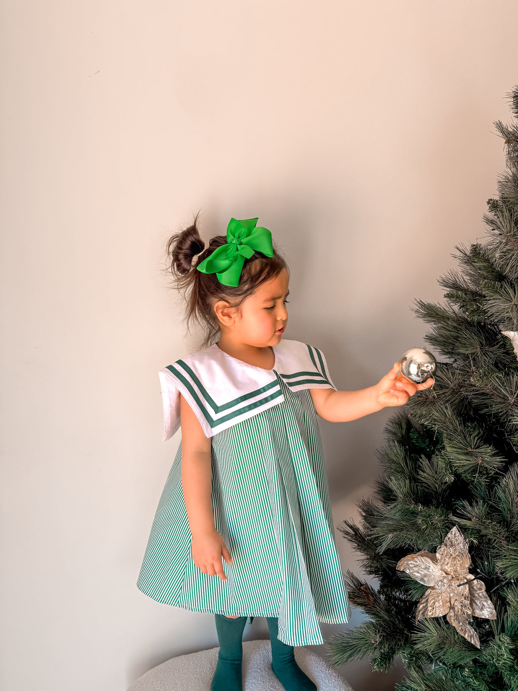 Young girl in a green and white dress decorating a Christmas tree.