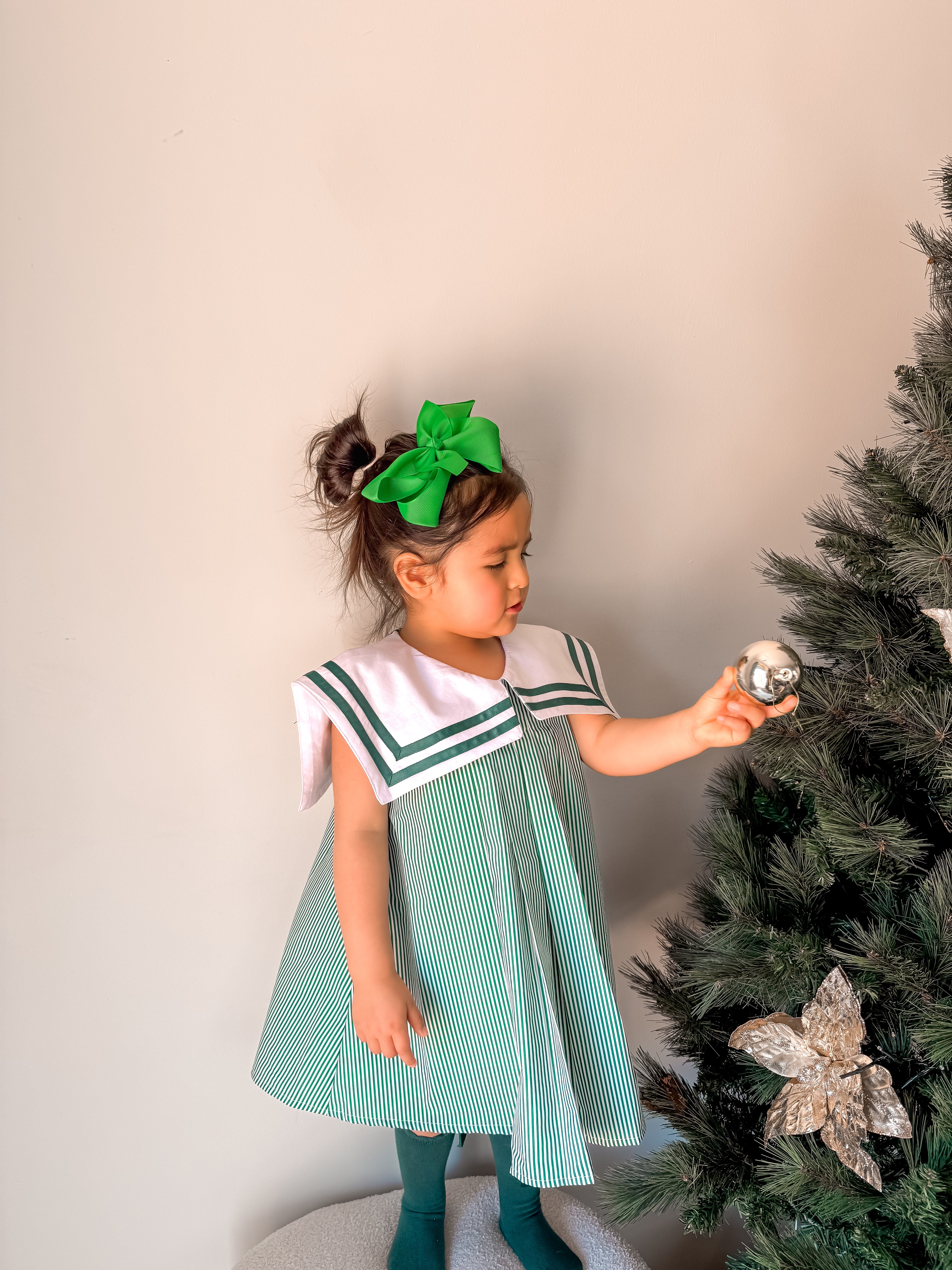 Young girl in a green and white dress decorating a Christmas tree.