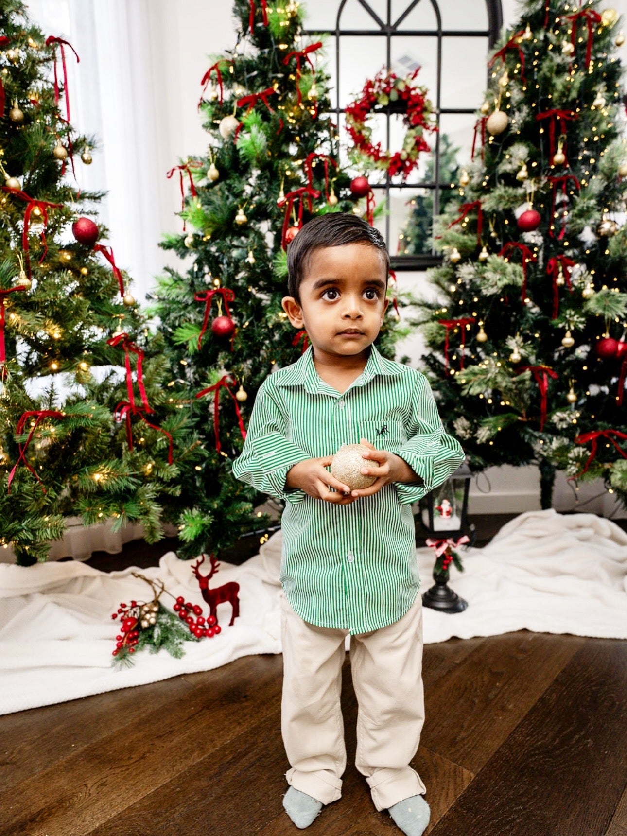 front profile photo- full shot of a toddler boy wearing a white and green shirt with MAR embroidery on the pocket with white/cream pants in front of Christmas trees
