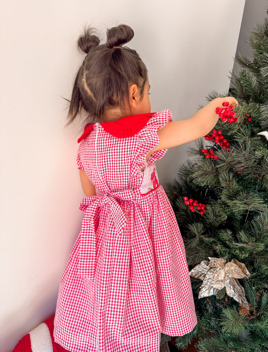 Child in a red checkered dress decorating a Christmas tree.