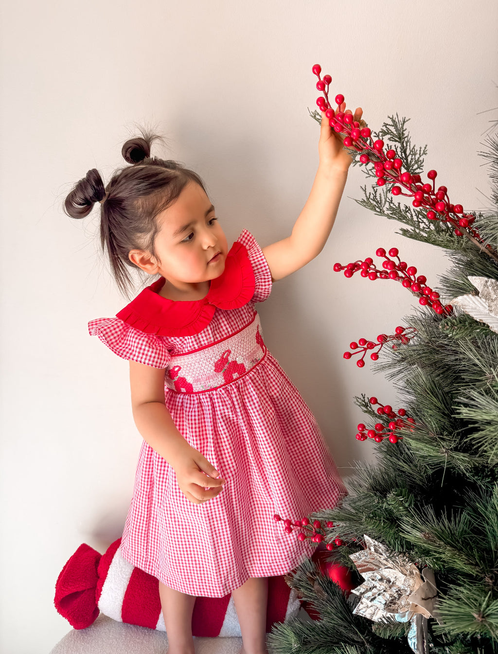 Child in a red and pink dress decorating a Christmas tree with red berries.