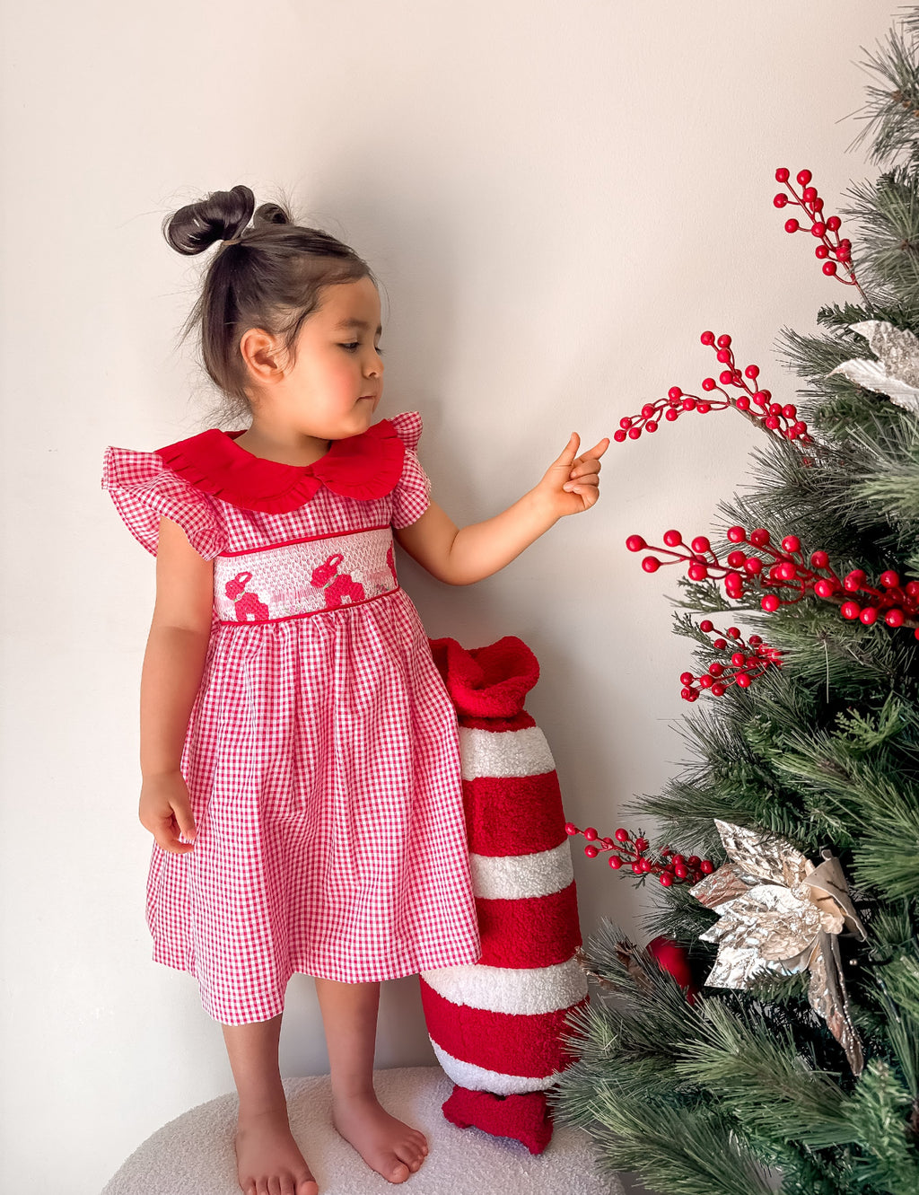 Child in a red dress standing next to a Christmas tree with decorations.