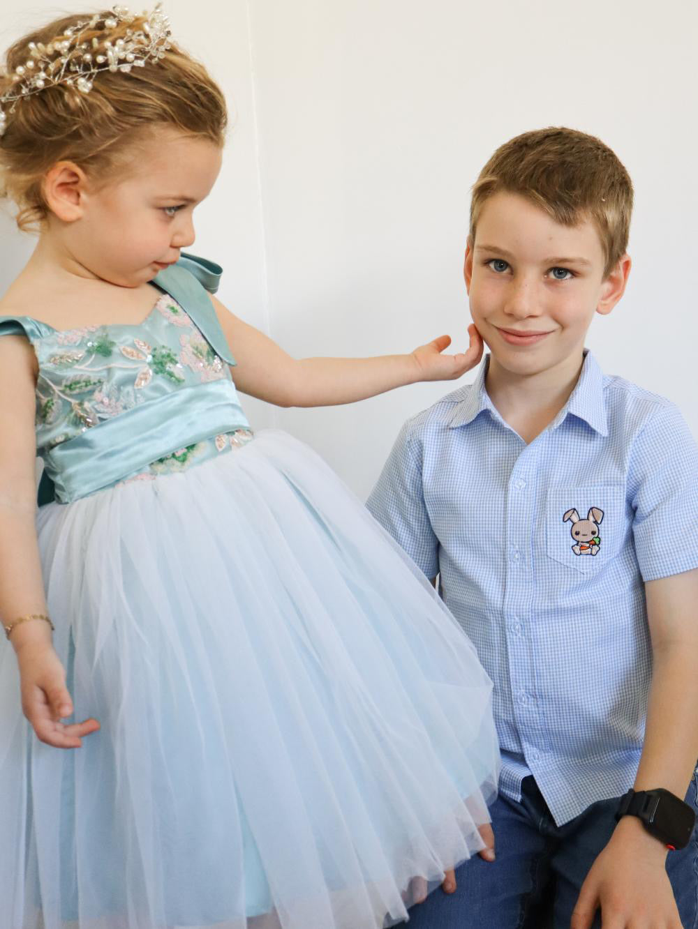 Two children, a girl in a light blue dress and a boy in a light blue shirt with a rabbit emblem, sitting together.