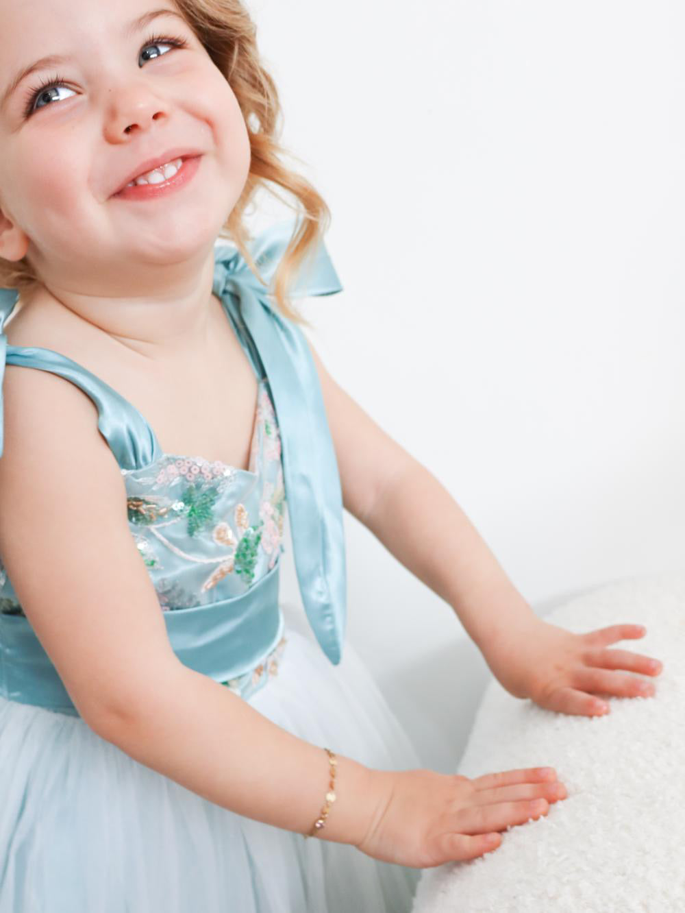 Child in a light blue dress with a bow sitting on a white surface.