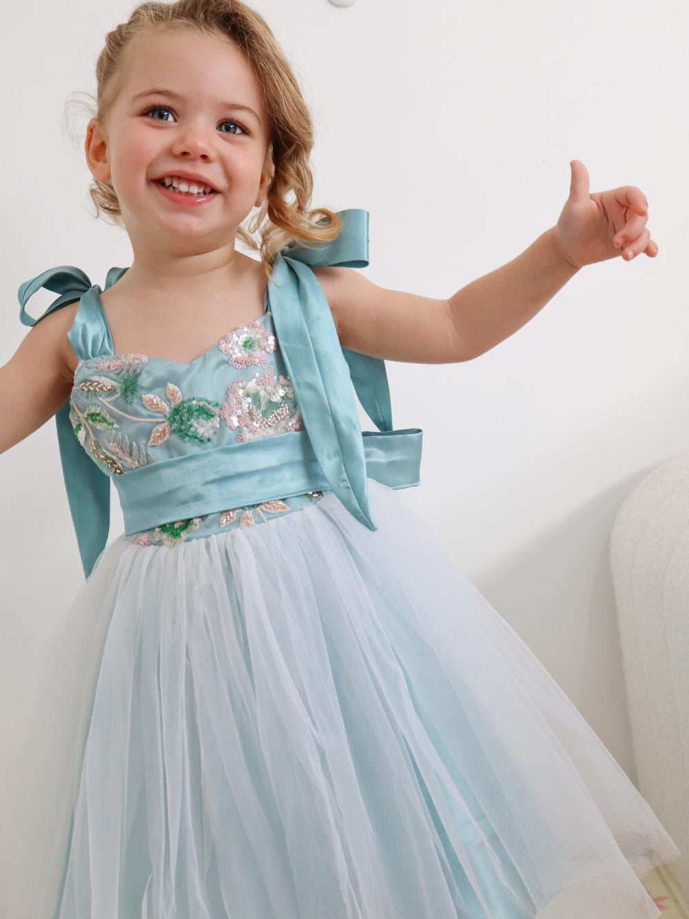 Child wearing a light blue floral dress with a bow on a white background