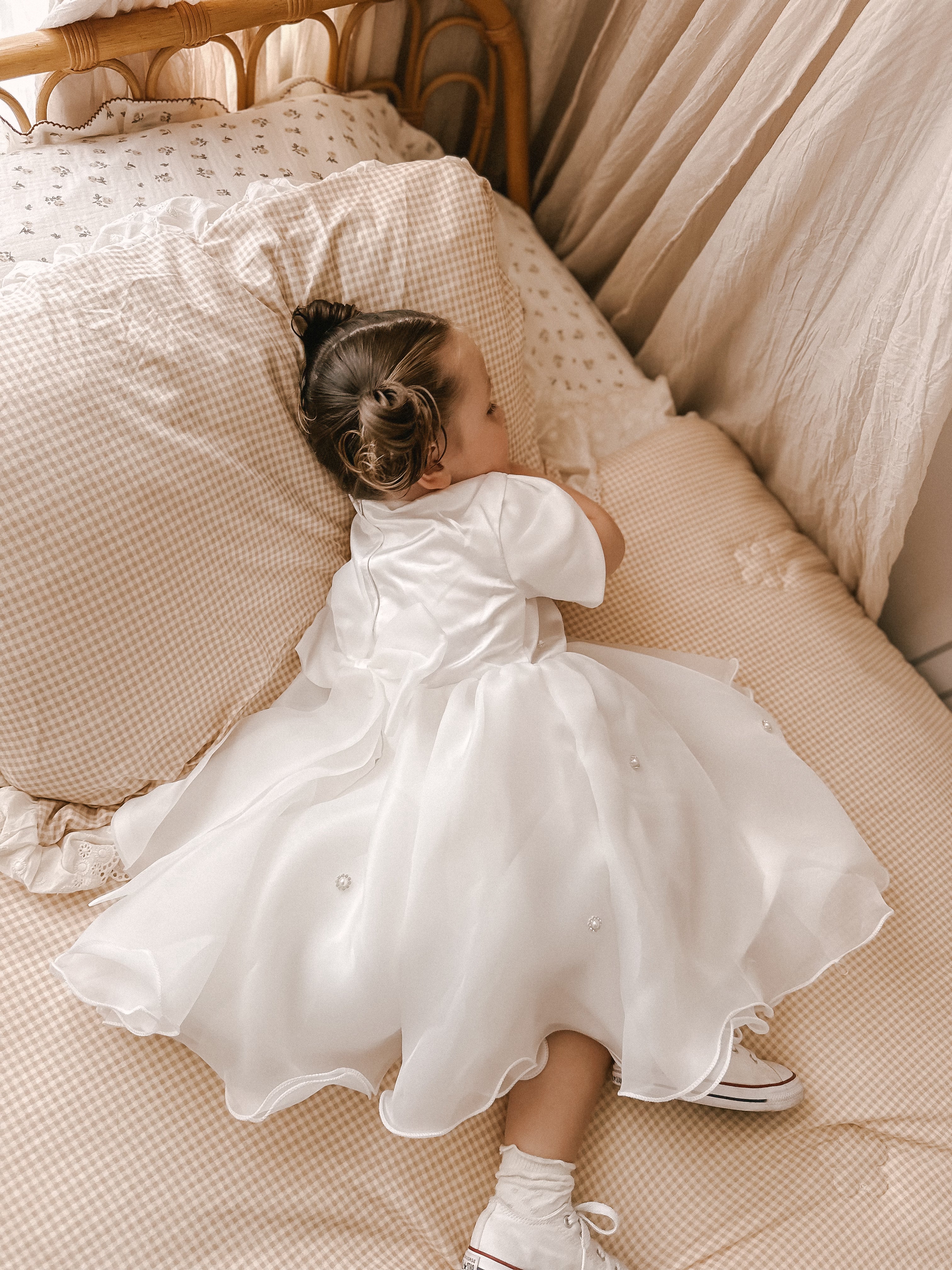 Young girl in a white dress lying on a bed with beige bedding