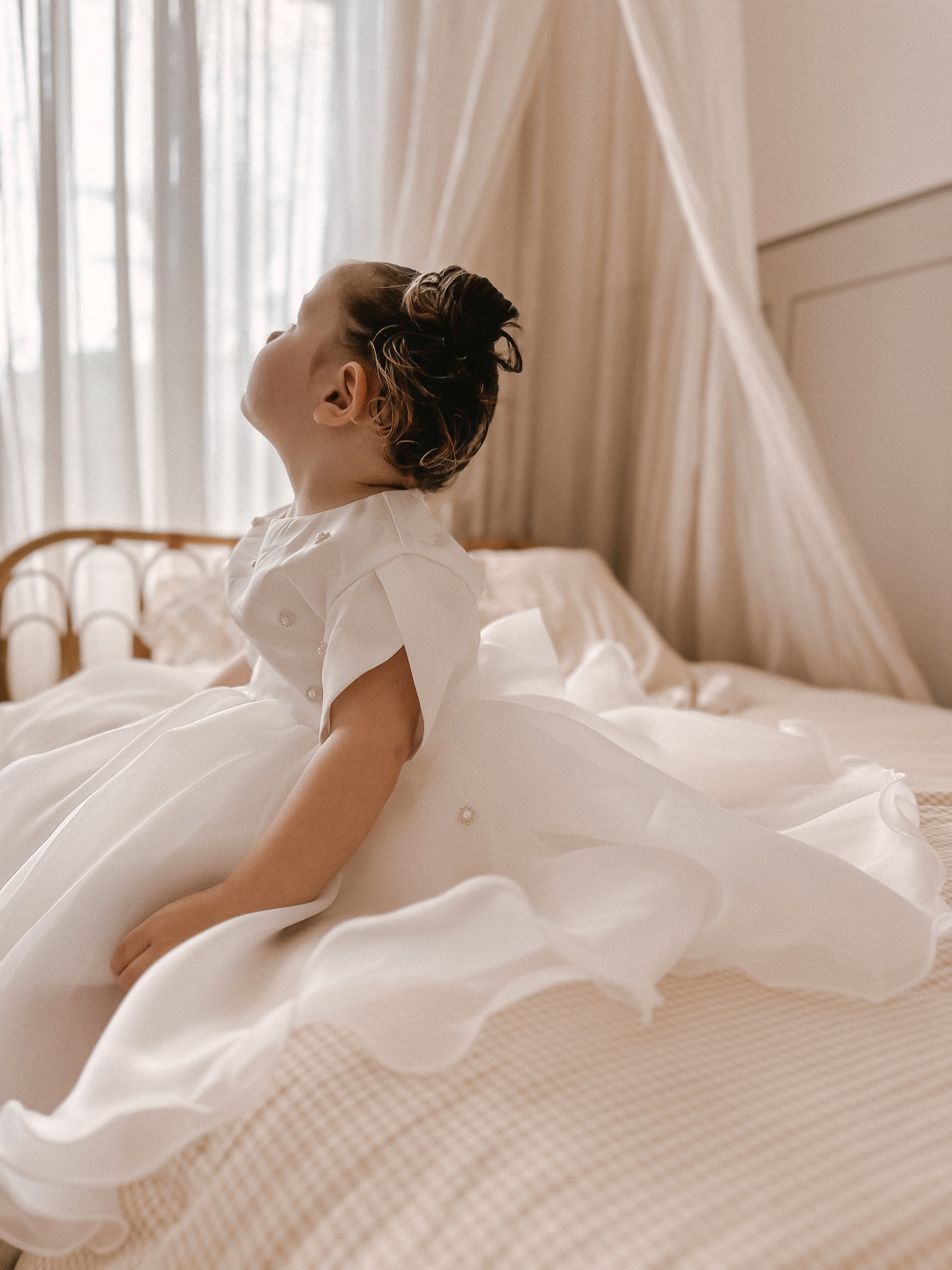 Child in a white dress sitting on a bed with a canopy