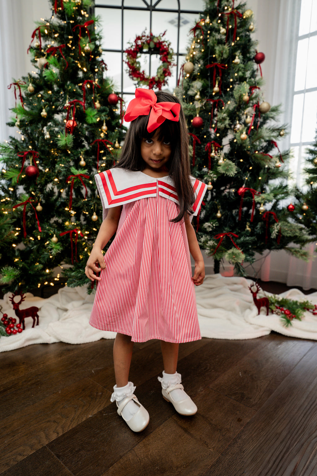 Young girl in a red and white dress standing in front of Christmas trees.