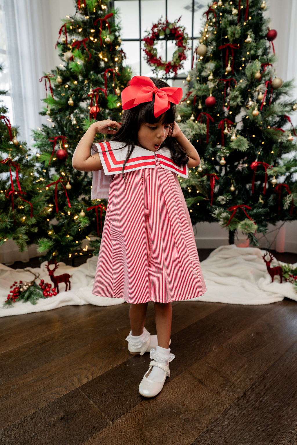 Young girl in a red and white dress standing in front of Christmas trees.