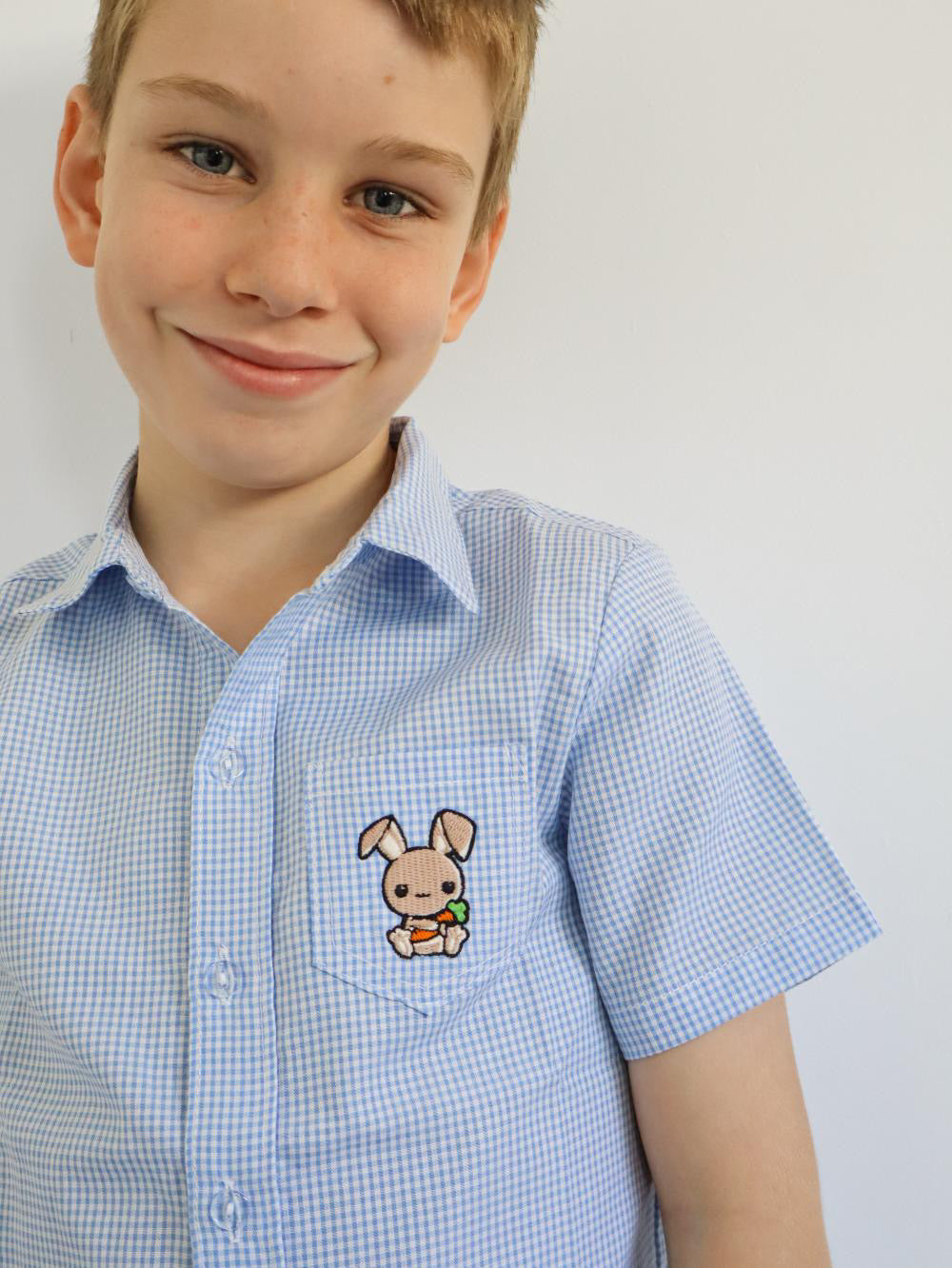 boy in a white and blue gingham shirt made of cotton with a cute embroidered bunny on the side pocket. short sleeve